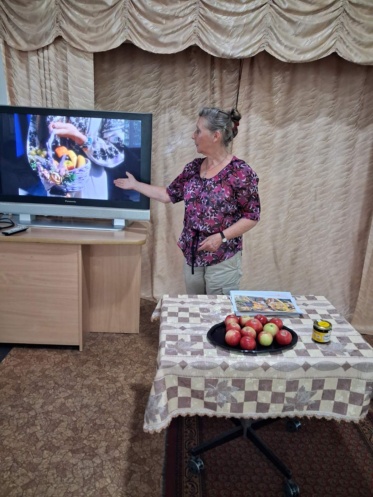 Яблука, мед на столі, жінка показує рукою в телевізор
