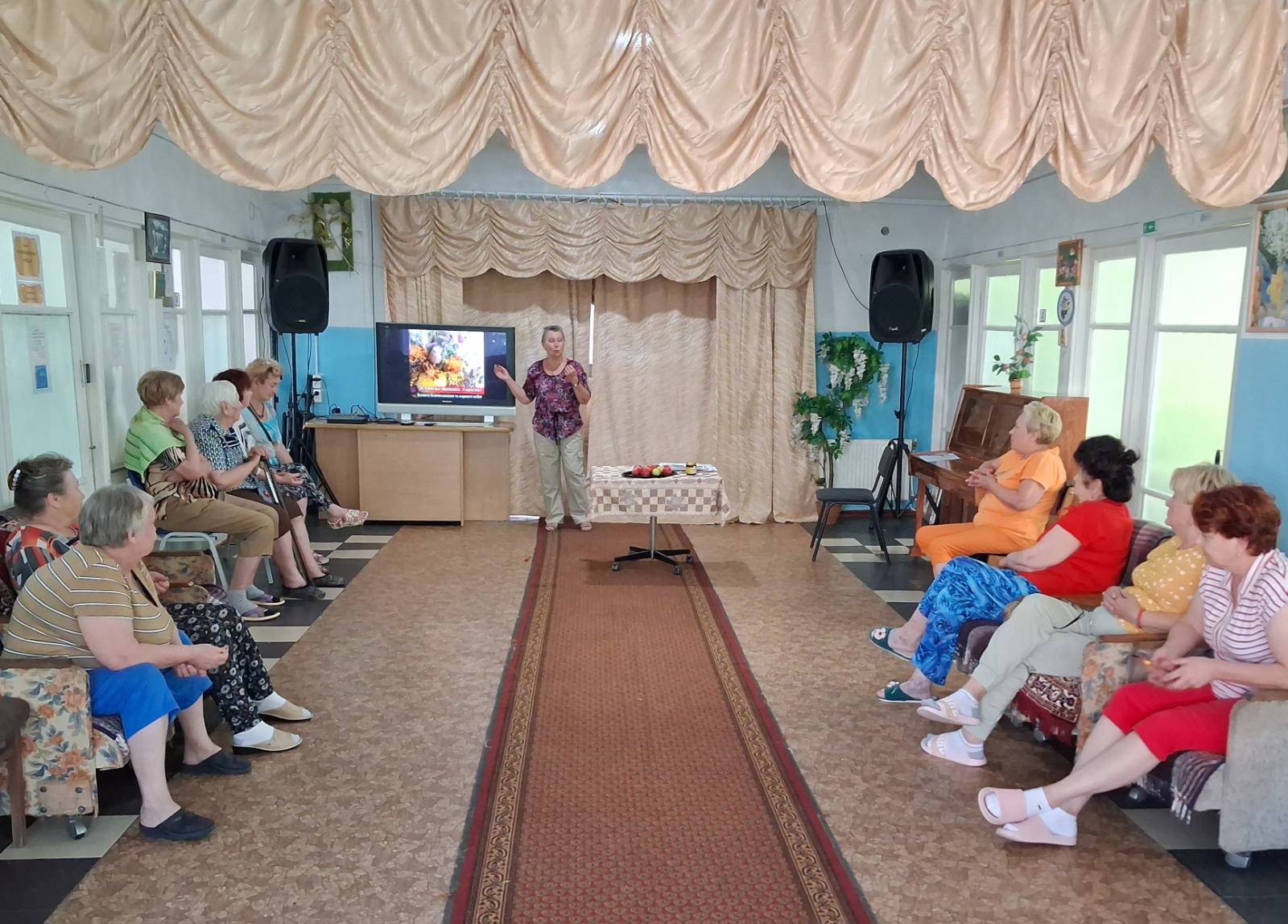 Люди в приміщенні, жінка показує рукою в телевізор